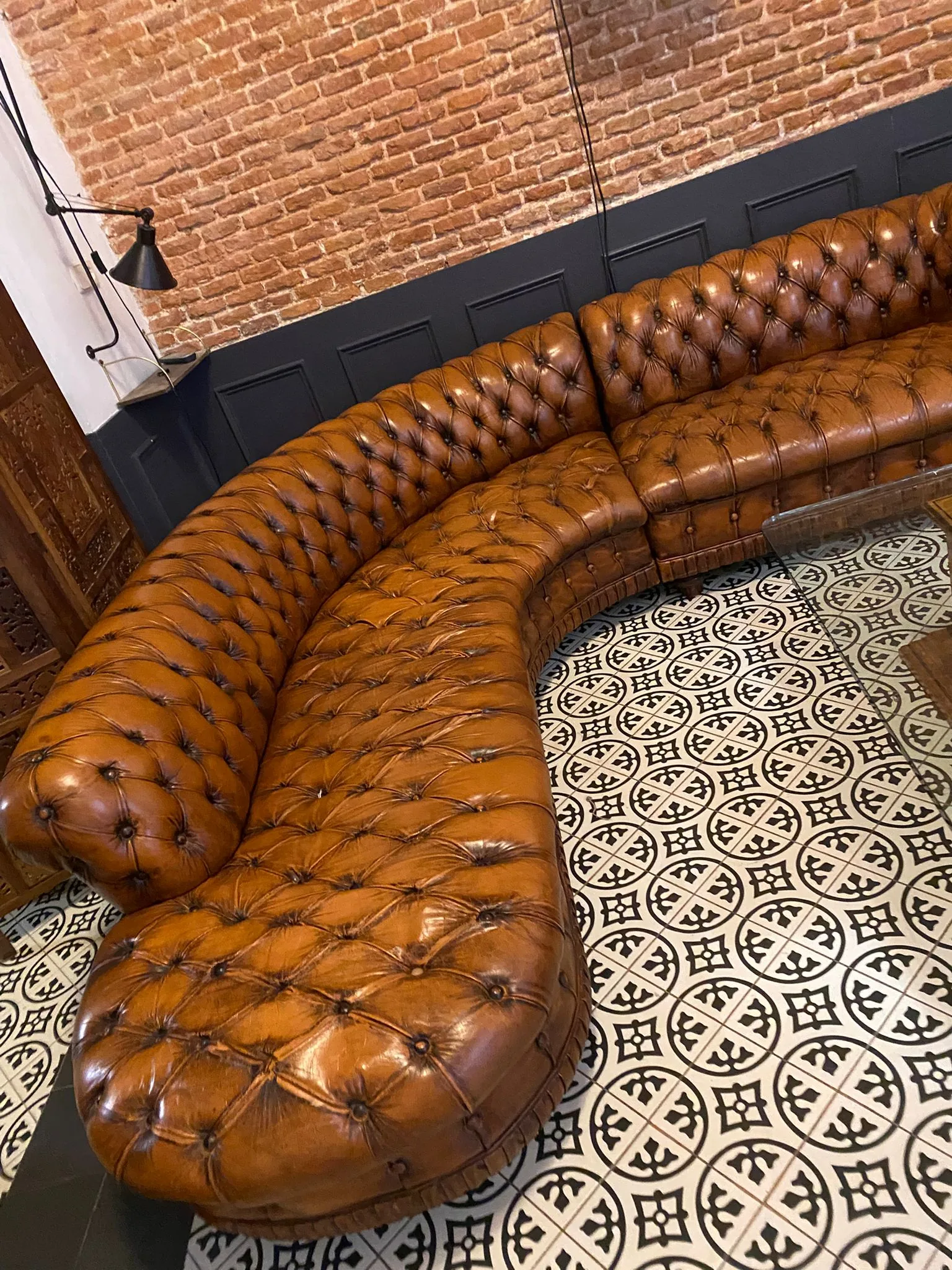 Sofá Chesterfield curvo en cuero cognac restaurado sobre suelo hidráulico